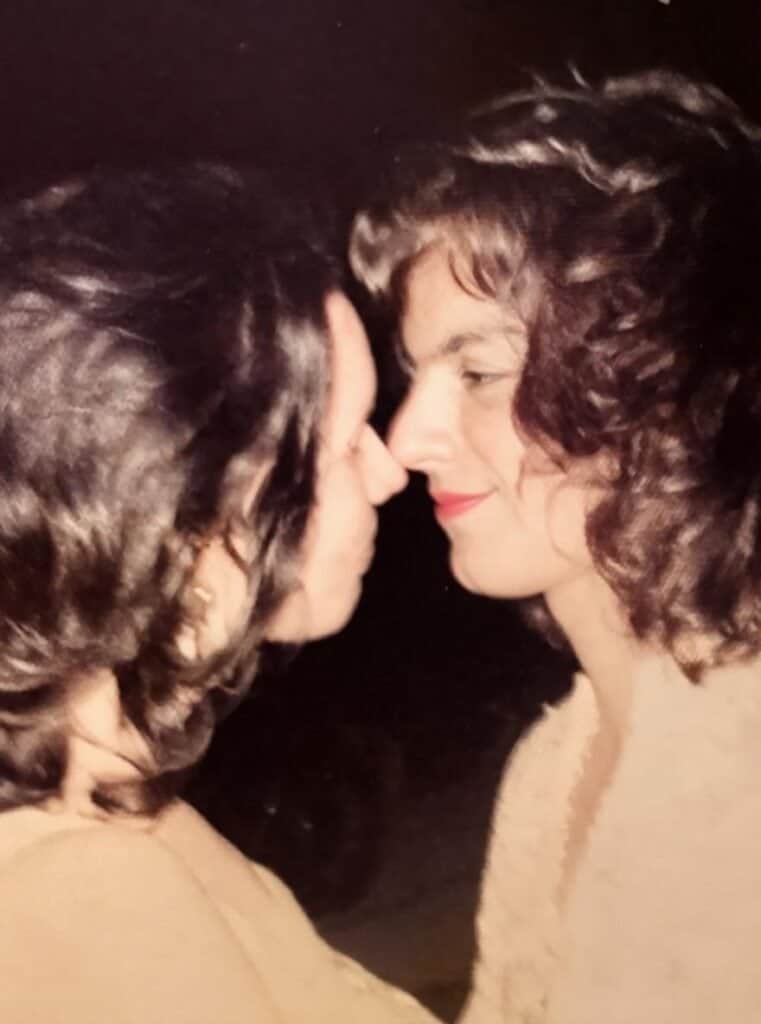Two women with curly hair touching noses, expressing affection.